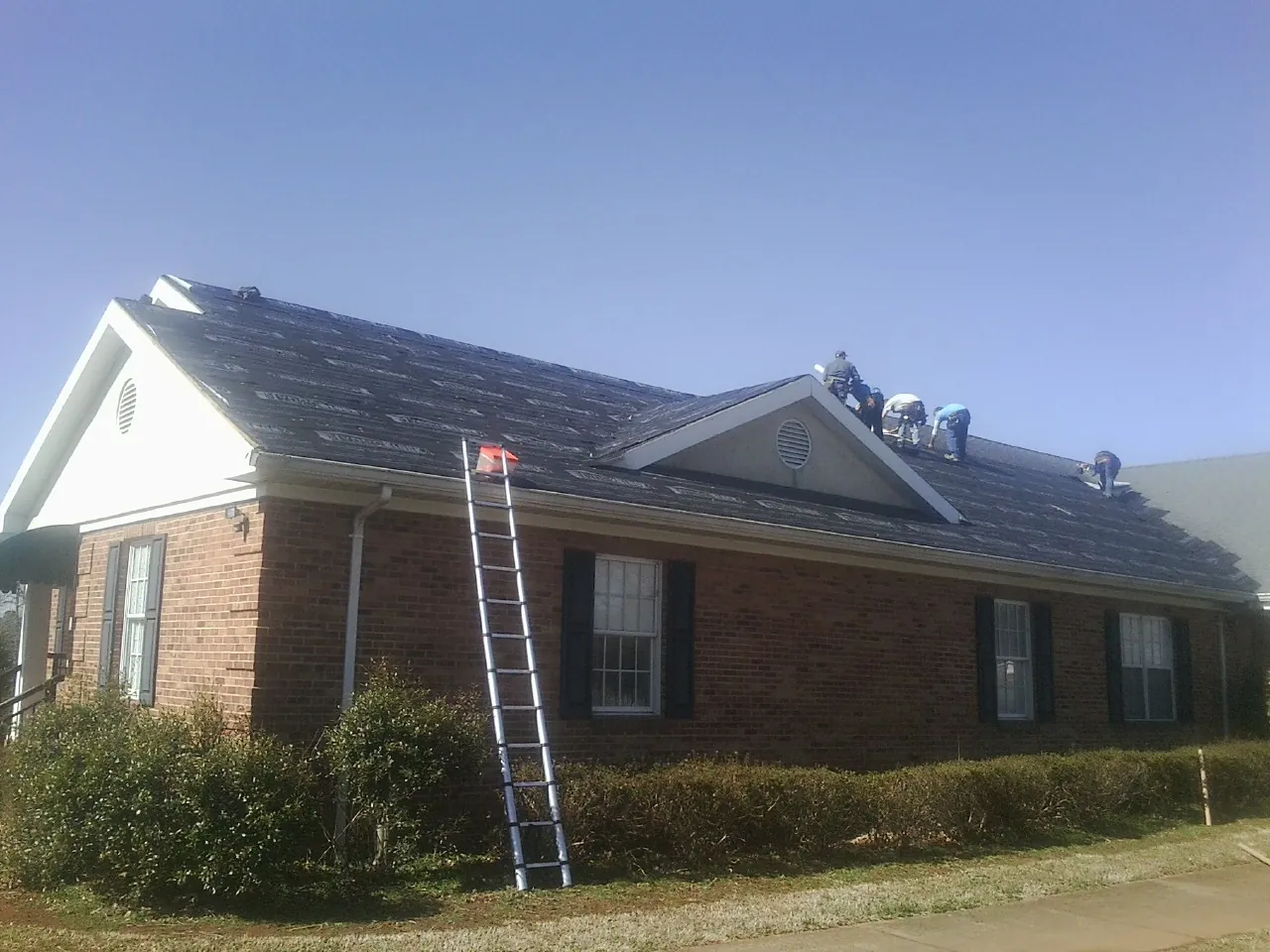 Crew tearing shingles off a brick ranch roof with a ladder set — Metal Roof Repair work by our crew in Hiwassee