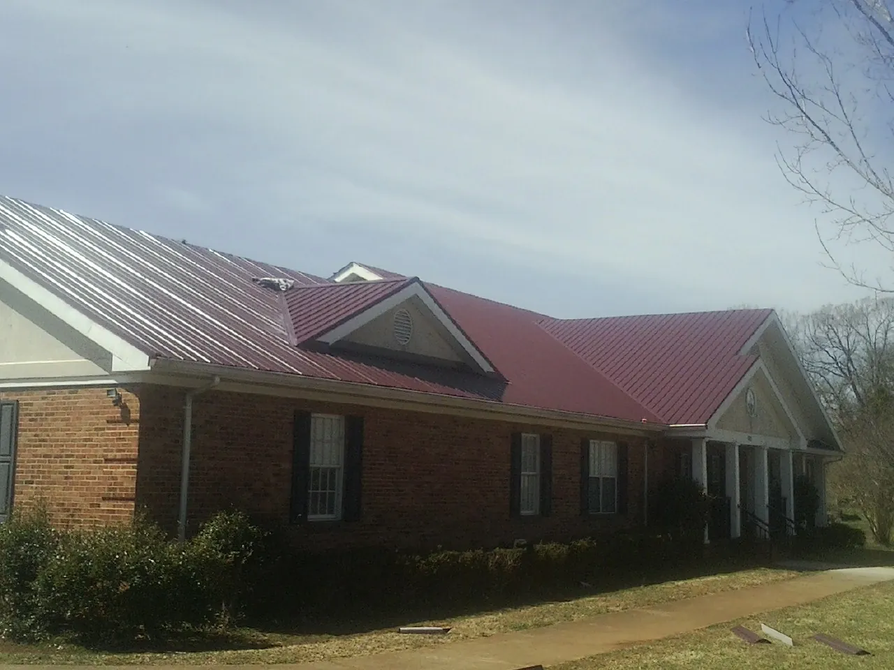 Red metal roof with gabled entries on a long brick building, from a Hail Damage Roof Repair job in Hiwassee