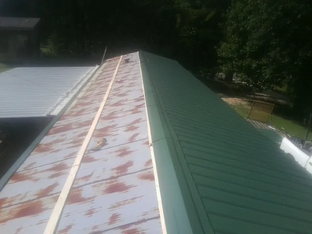 Old rusted panels beside newly installed green metal roofing — Wind Damage Roof Repair by Roofing Brothers in Hiwassee