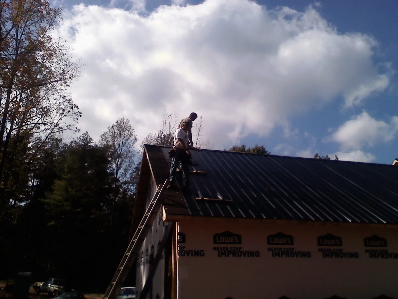 Roofer fastening dark metal panels high against a cloudy sky, from a Roof Inspection job in Hiwassee