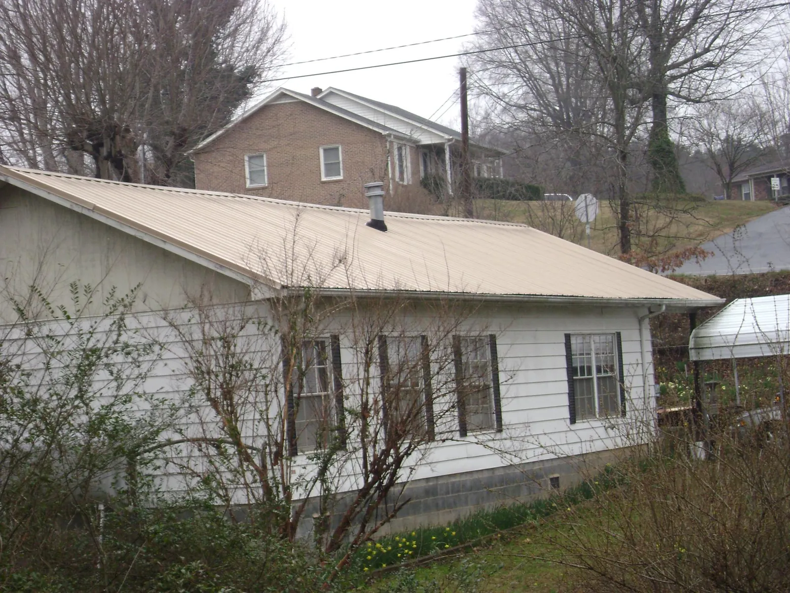 Tan metal roof on a white sided house set into a hillside — Commercial Roofing by Roofing Brothers in Hiwassee