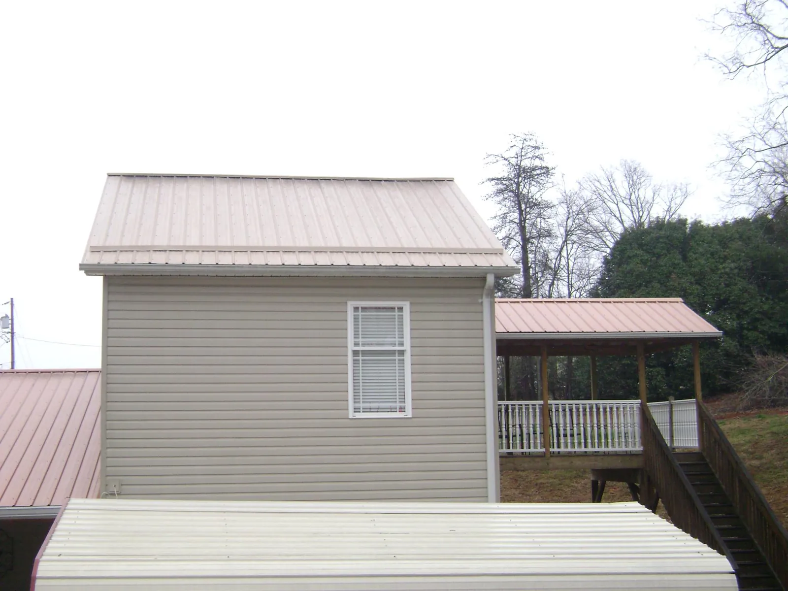 Tan metal roofs on a two story addition and attached porch, from a Roof Replacement job in Hiwassee